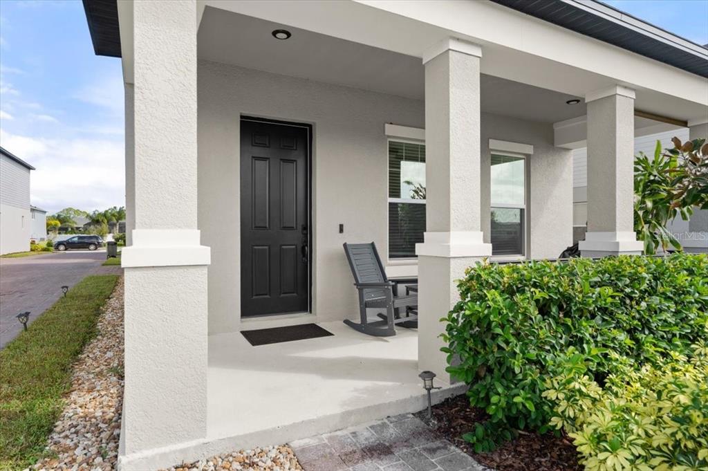 A covered front porch features a black door, a gray rocking chair, and stone pillars — 2916 MELETO BOULEVARD, NEW SMYRNA BEACH, FL