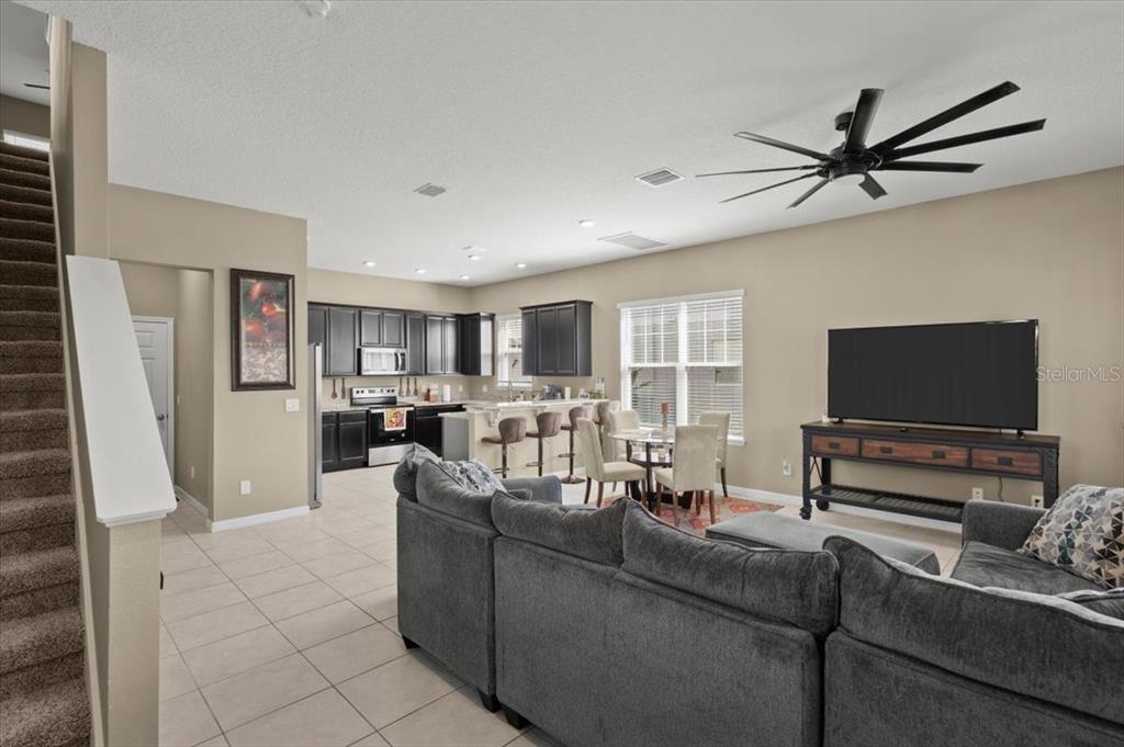 An open-concept living room and kitchen feature dark cabinetry, tile flooring, and a sectional sofa — 2916 MELETO BOULEVARD, NEW SMYRNA BEACH, FL