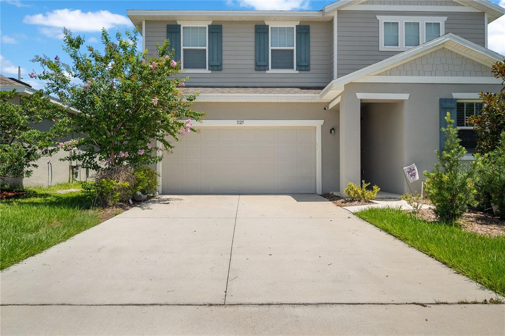 A two-story suburban house features a concrete driveway, a two-car garage, and gray siding — 1125 MATTIE POINTE BOULEVARD, AUBURNDALE, FL