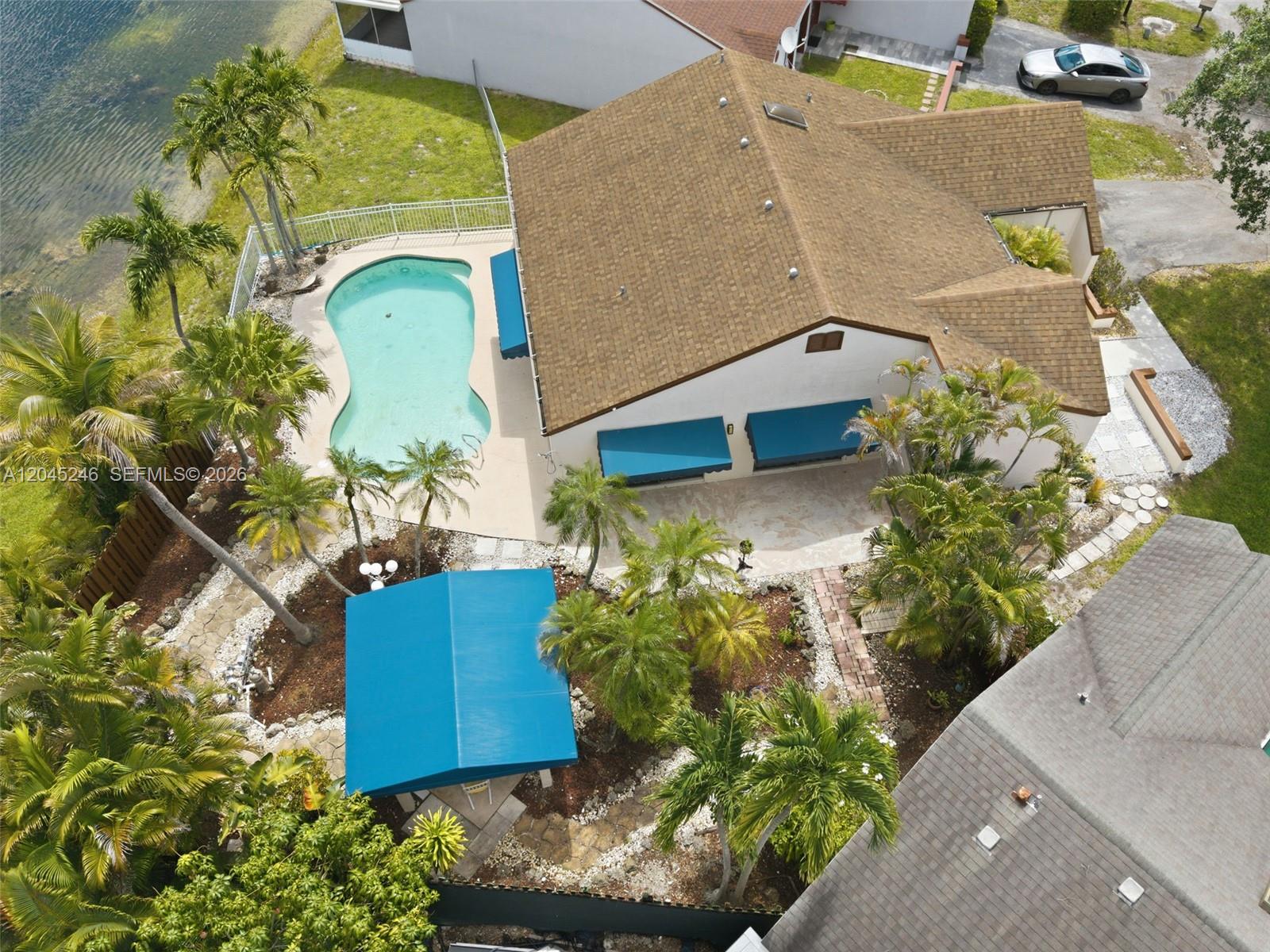 An aerial view shows a house with a pool, blue awnings, and palm trees — 8165 NW 187th Ter, Hialeah FL 33015, HIALEAH, FL
