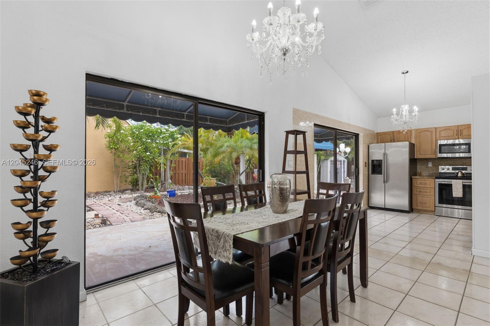 A dining area with a wooden table, chandelier, and sliding doors opening to a patio — 8165 NW 187th Ter, Hialeah FL 33015, HIALEAH, FL