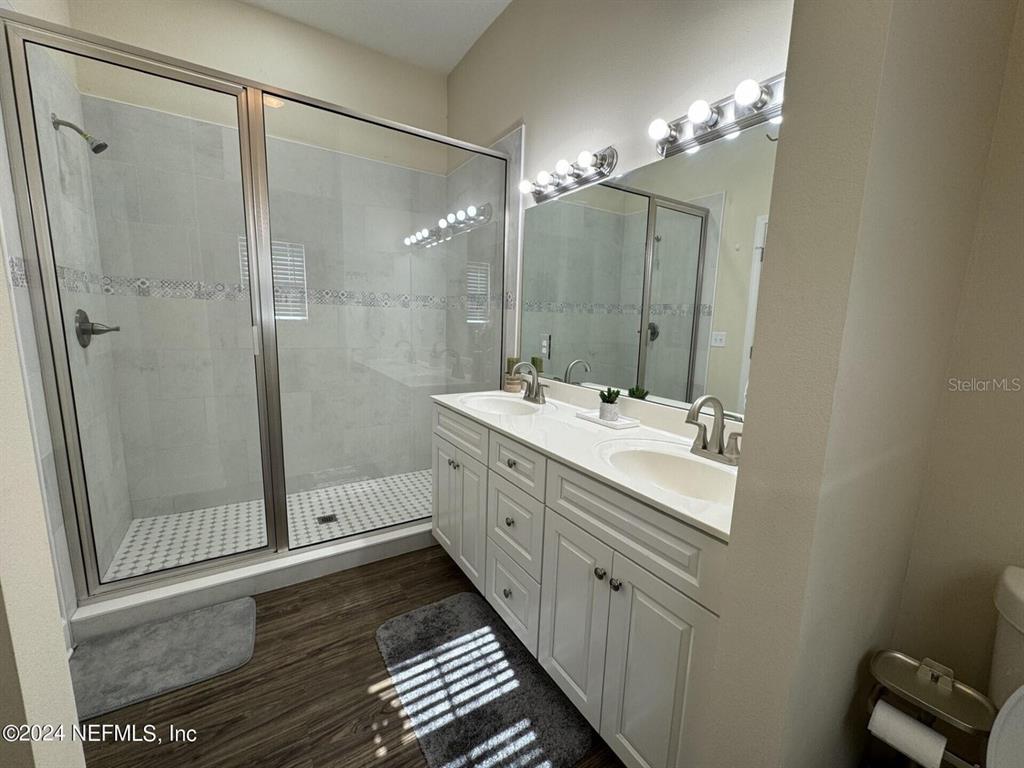 A bathroom features a glass-enclosed shower, a double vanity with white cabinets, and wood-look flooring — 6107 W 1ST MNR, PALATKA, FL
