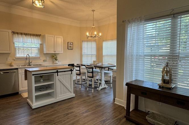 A kitchen features white cabinets, a sliding-door island, a dining table, and wood-look flooring — 6107 W 1ST MNR, PALATKA, FL