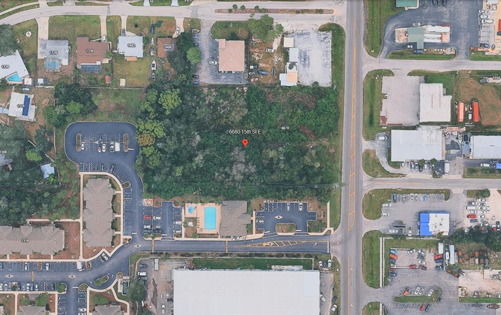 This aerial view shows a wooded, undeveloped rectangular lot situated between commercial and residential properties — 6680 15TH STREET E, SARASOTA, FL