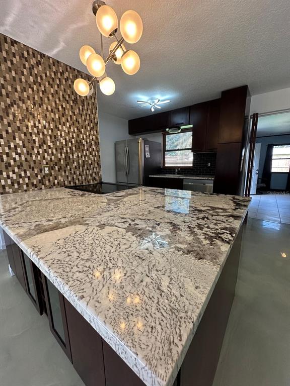 A kitchen features a large granite-topped island, dark cabinetry, and a mosaic tile accent wall — 1508 MONA AVENUE, OCOEE, FL