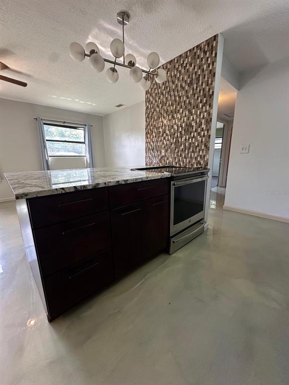 A kitchen island with dark cabinets and a granite countertop sits beneath a modern chandelier — 1508 MONA AVENUE, OCOEE, FL