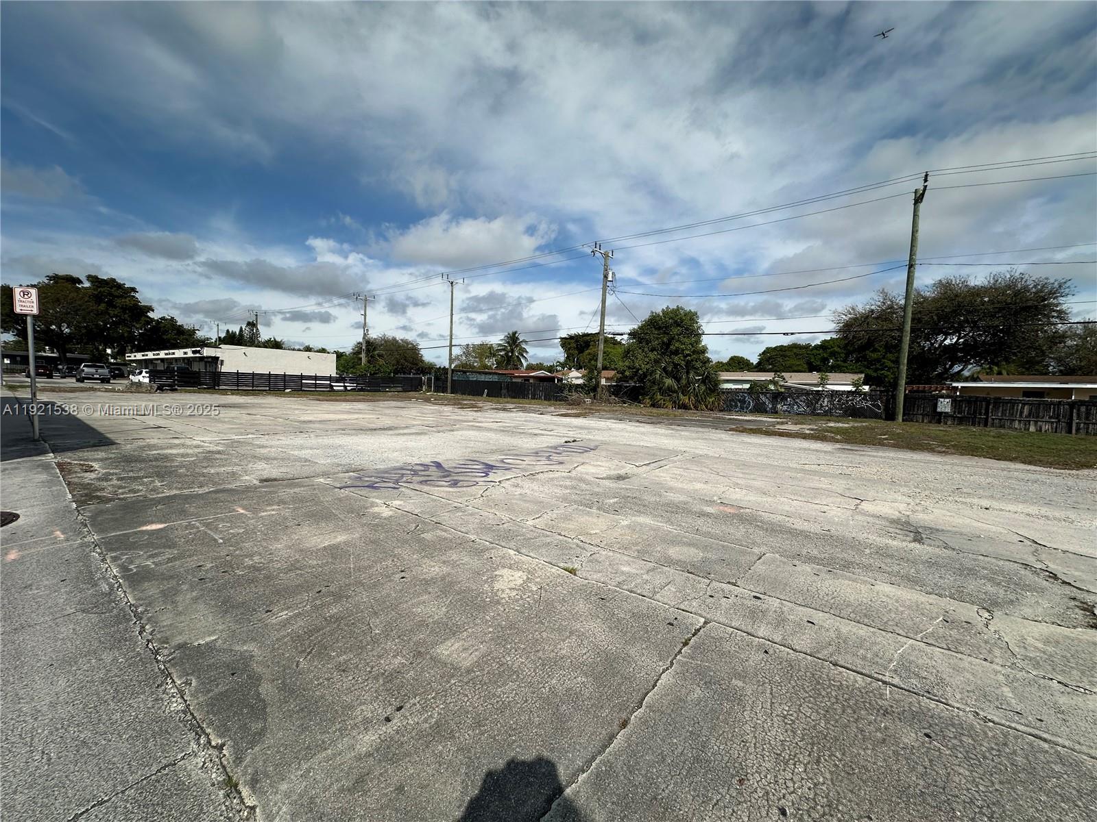 A large, vacant concrete lot is enclosed by a fence under a cloudy sky — 6501 Pembroke Rd, Hollywood FL 33023, HOLLYWOOD, FL