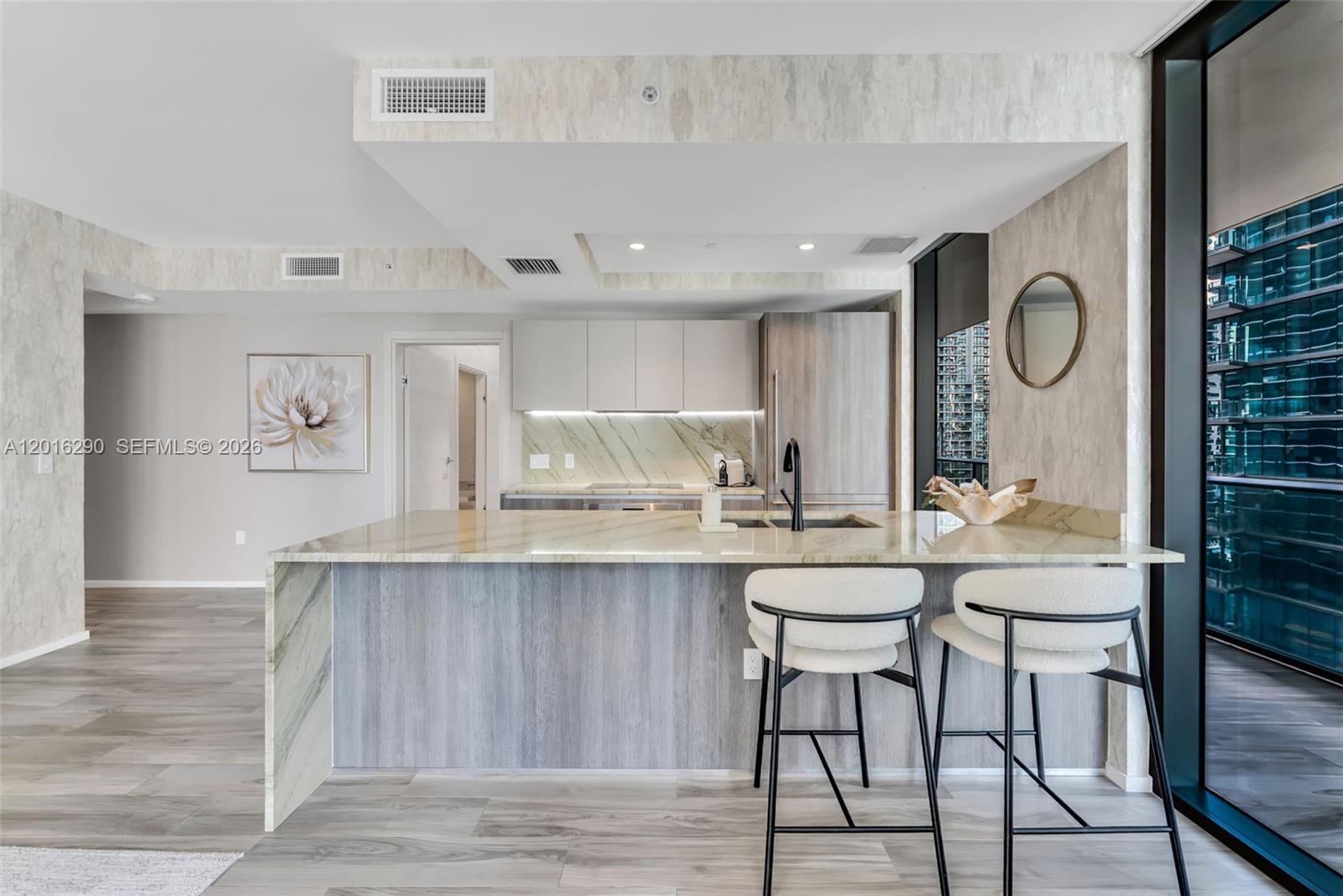 A modern kitchen features a marble waterfall island, light wood cabinetry, and two bar stools — 801 S Miami Ave # 1805, Miami FL 33130, MIAMI, FL