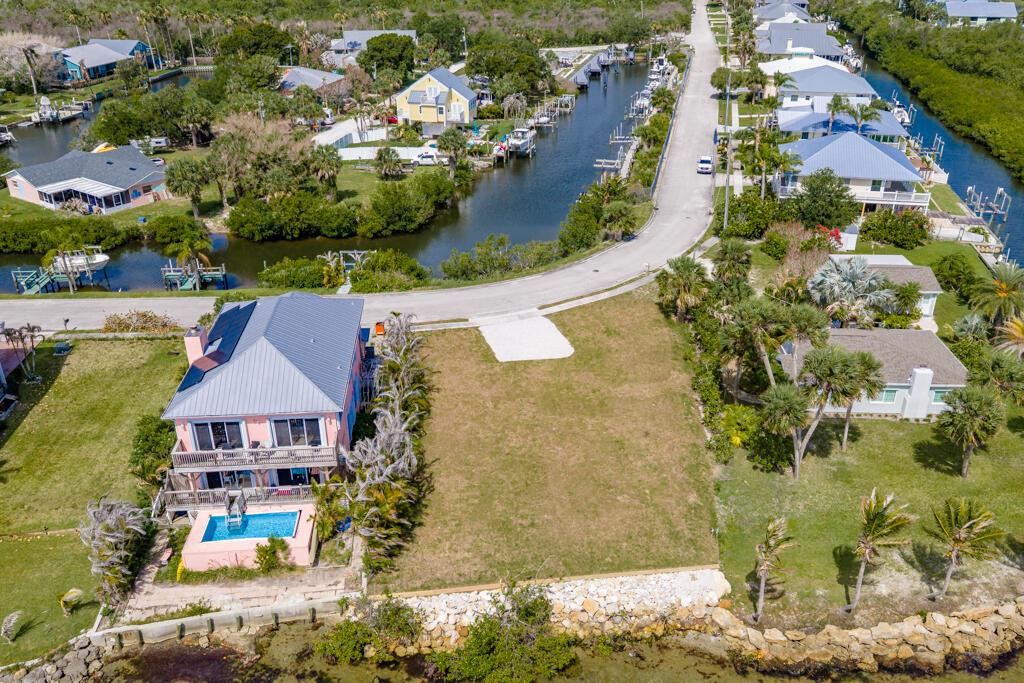 An aerial view shows a pink waterfront house with a pool next to a vacant lot — SEBASTIAN, FL