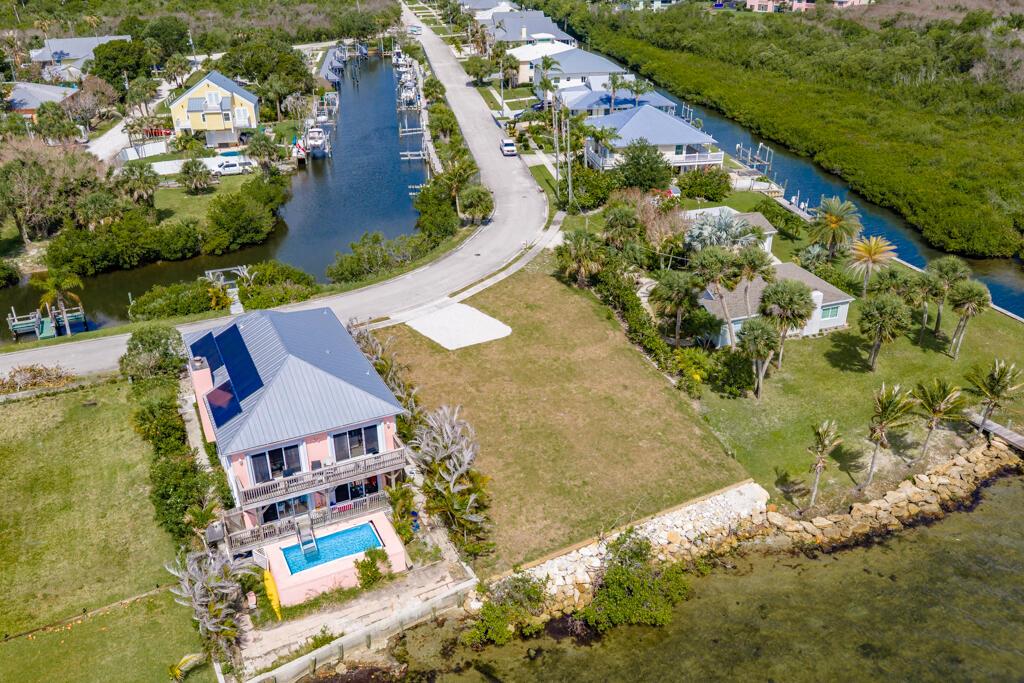 An aerial view shows a pink waterfront house with a pool next to a vacant lot — SEBASTIAN, FL