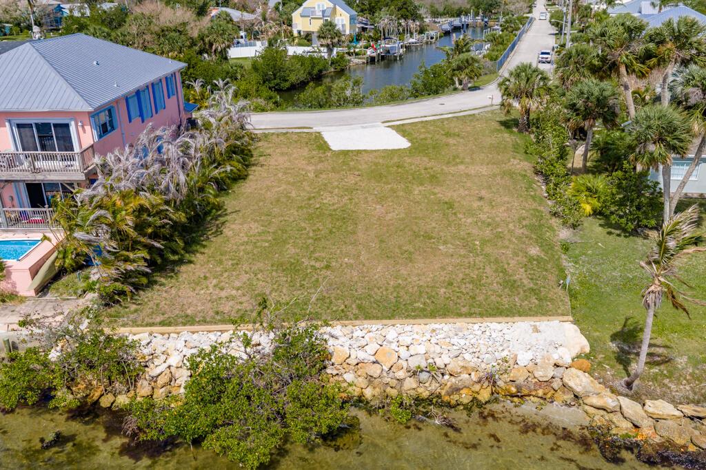 An aerial view shows a vacant waterfront lot with a stone seawall and adjacent house — SEBASTIAN, FL