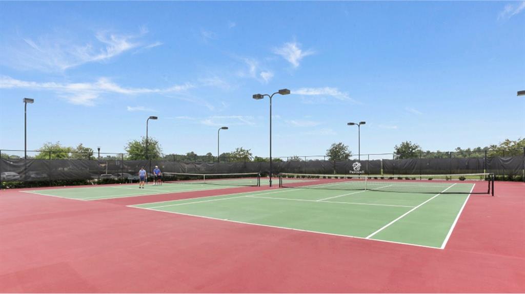 Two outdoor tennis courts with green surfaces and red borders are surrounded by black fencing — 6053 MEDITATION DRIVE, CLERMONT, FL