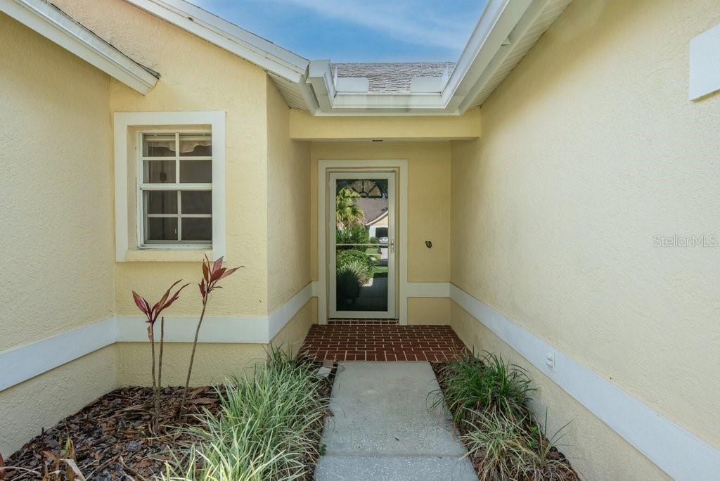 A concrete walkway leads to the front entrance of a yellow house with a screen door — 17610 ESPRIT DRIVE, TAMPA, FL