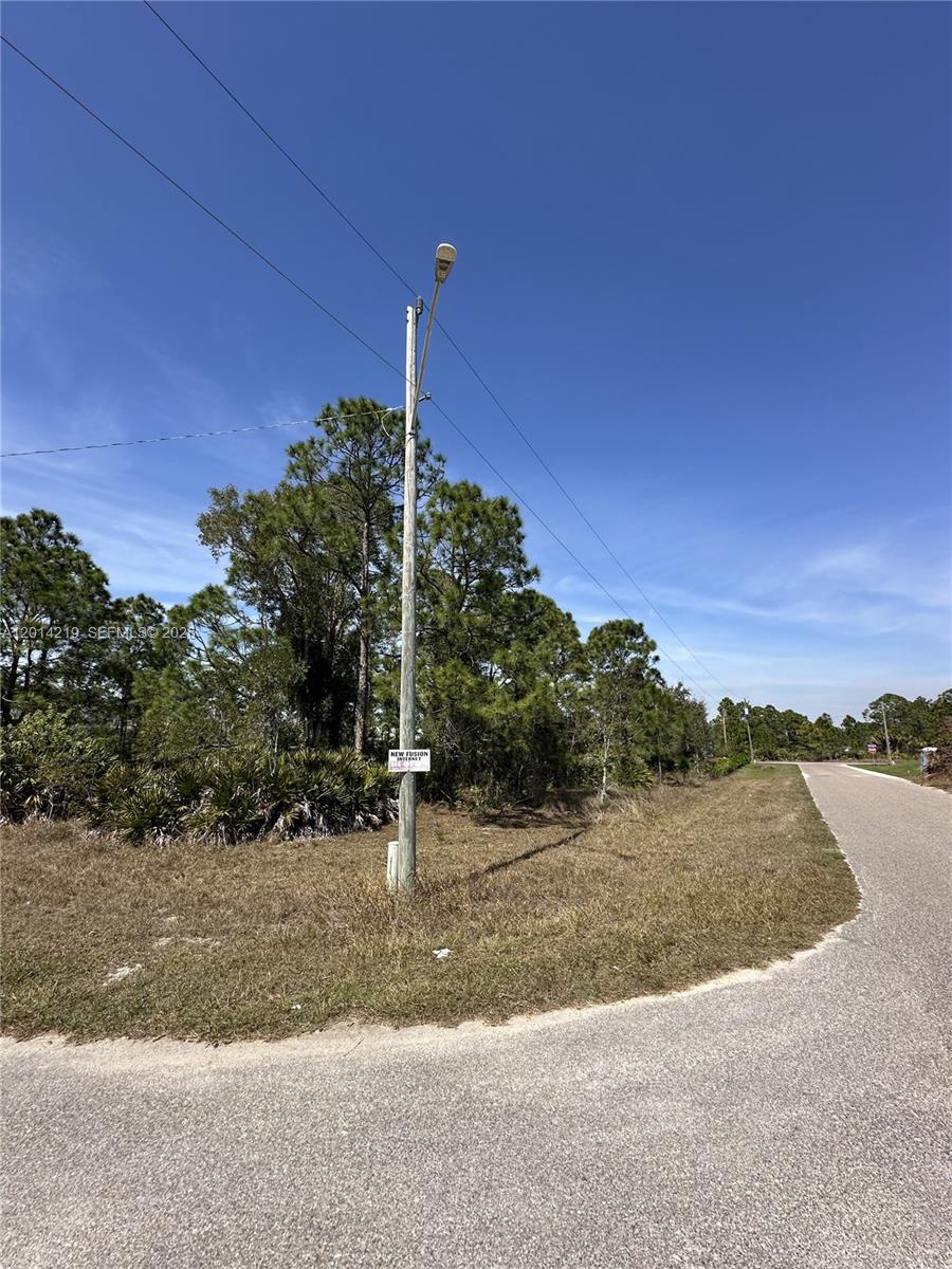 A utility pole stands on a grassy corner lot next to a paved road — 2900 33rd St W, Lehigh Acres FL 33971, LEHIGH ACRES, FL