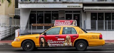 A yellow taxi with advertisements for Club Madonna is parked in front of a restaurant building — 1527 Washington Ave, Miami Beach FL 33139, MIAMI BEACH, FL