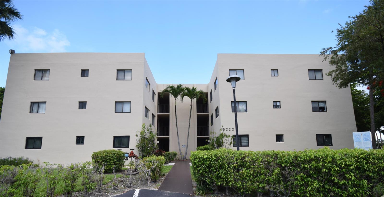 A three-story apartment building with a central walkway and palm trees in front — 5220 Las Verdes Circle # 220, Delray Beach FL 33484, DELRAY BEACH, FL