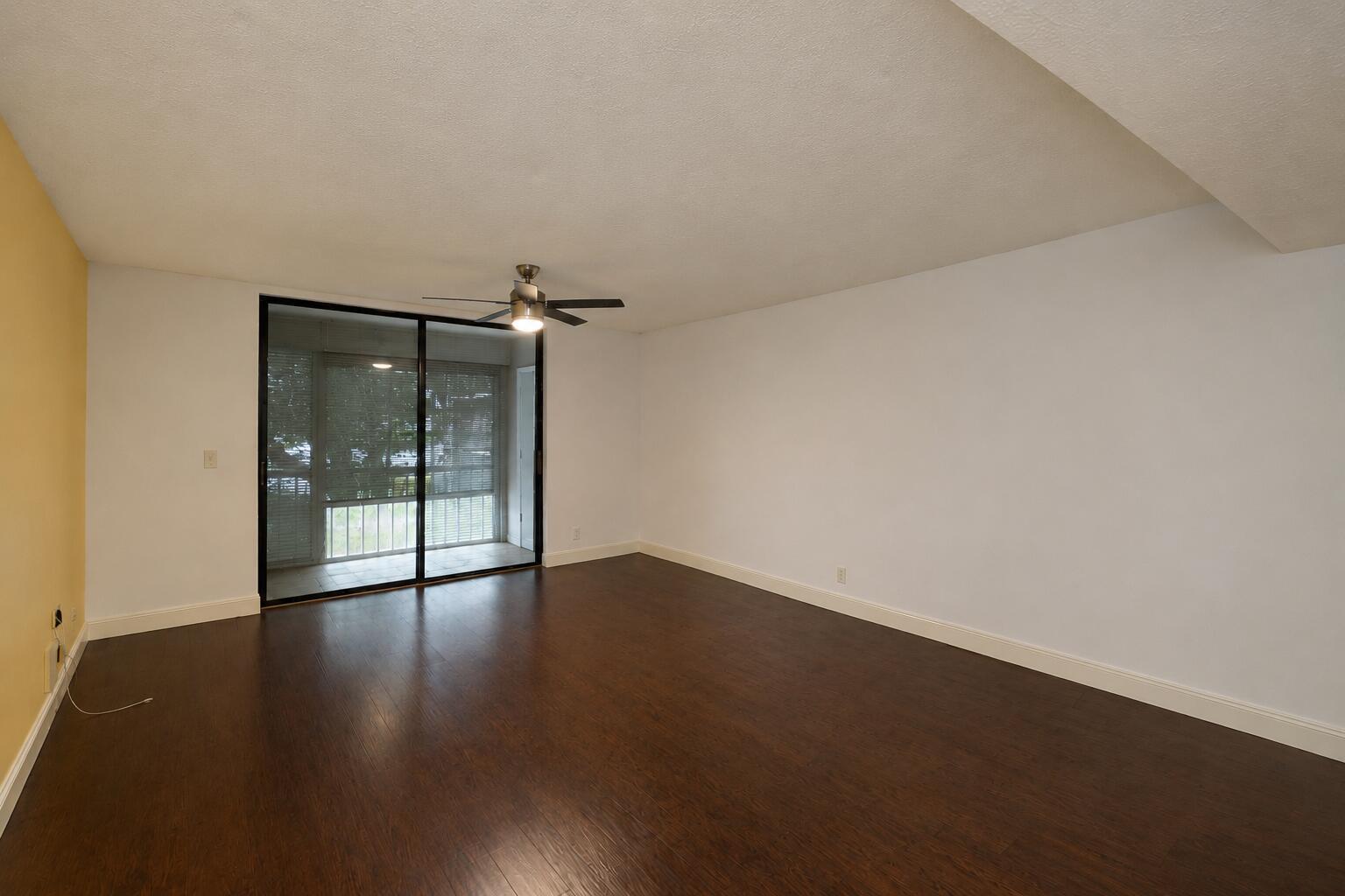 An empty room with dark wood flooring, white walls, a ceiling fan, and sliding glass doors — 5220 Las Verdes Circle # 220, Delray Beach FL 33484, DELRAY BEACH, FL