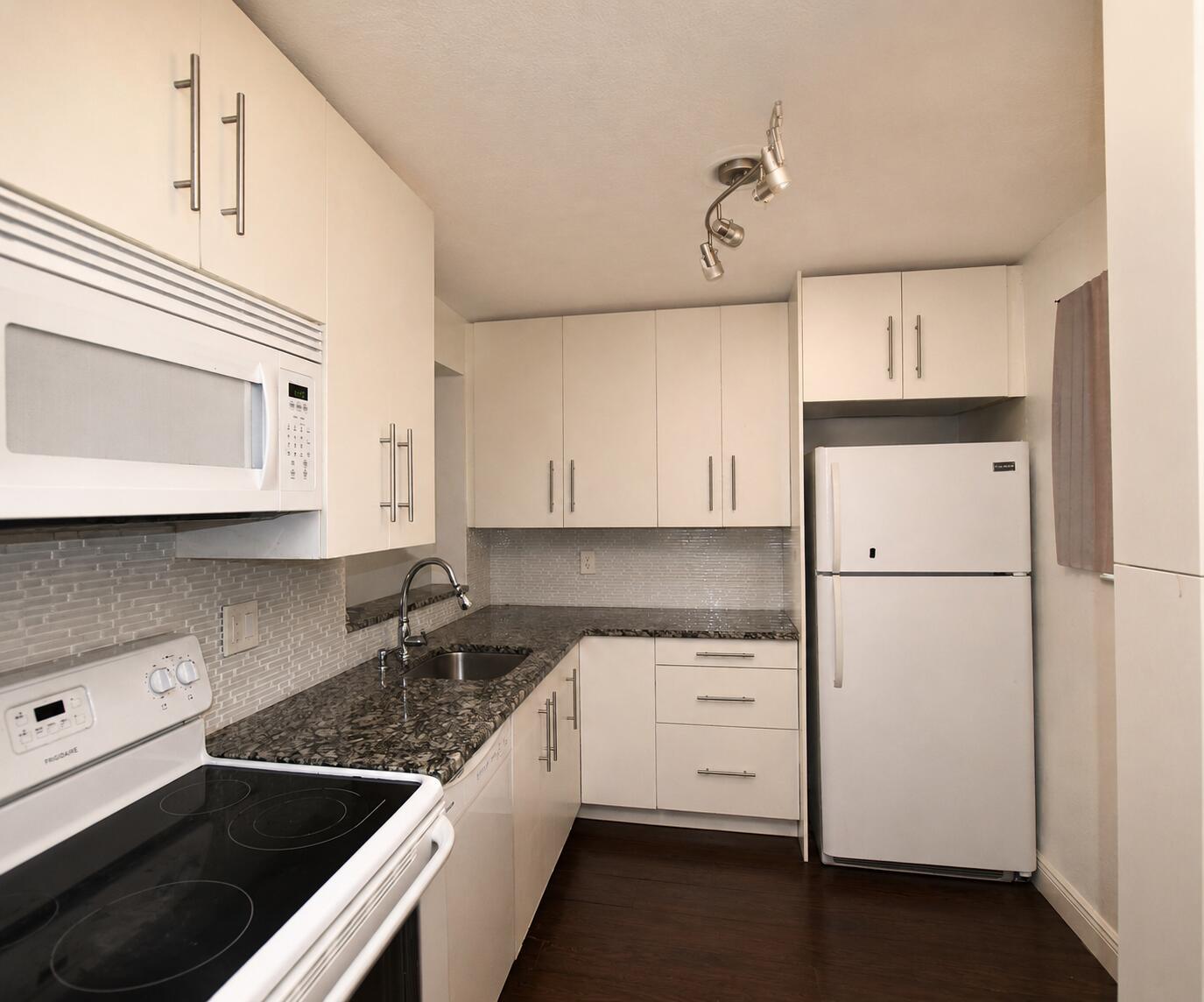 A kitchen with white cabinets, dark granite countertops, a white refrigerator, and a tiled backsplash — 5220 Las Verdes Circle # 220, Delray Beach FL 33484, DELRAY BEACH, FL