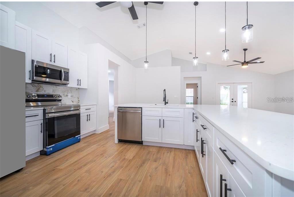 A modern kitchen features white cabinetry, stainless steel appliances, a large island, and wood flooring — 15909 GREEN COVE BOULEVARD, CLERMONT, FL