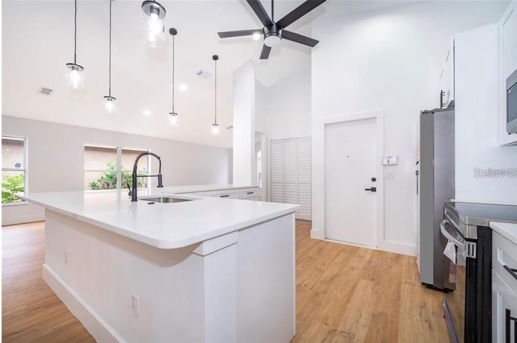 A modern kitchen features a white island with a sink, pendant lights, and wood flooring — 15909 GREEN COVE BOULEVARD, CLERMONT, FL