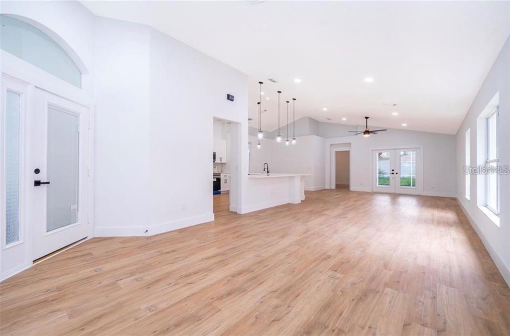 An open-concept living area features light wood flooring, white walls, and a kitchen island — 15909 GREEN COVE BOULEVARD, CLERMONT, FL