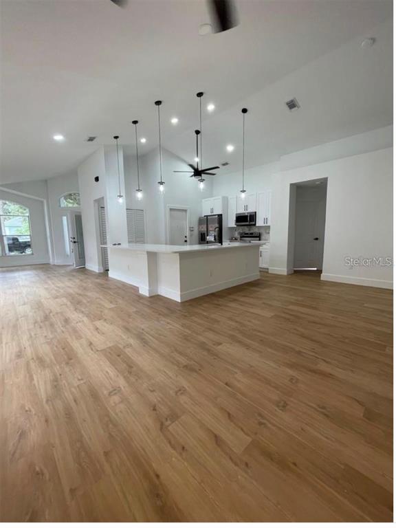 A bright, open-concept kitchen features a large white island, pendant lighting, and wood-look flooring — 15909 GREEN COVE BOULEVARD, CLERMONT, FL