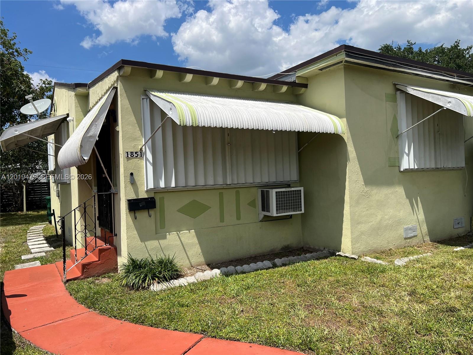 A pale yellow house exterior features metal awnings, a window air conditioner, and red steps — 1851 NW 51st Ter, Miami FL 33142, MIAMI, FL