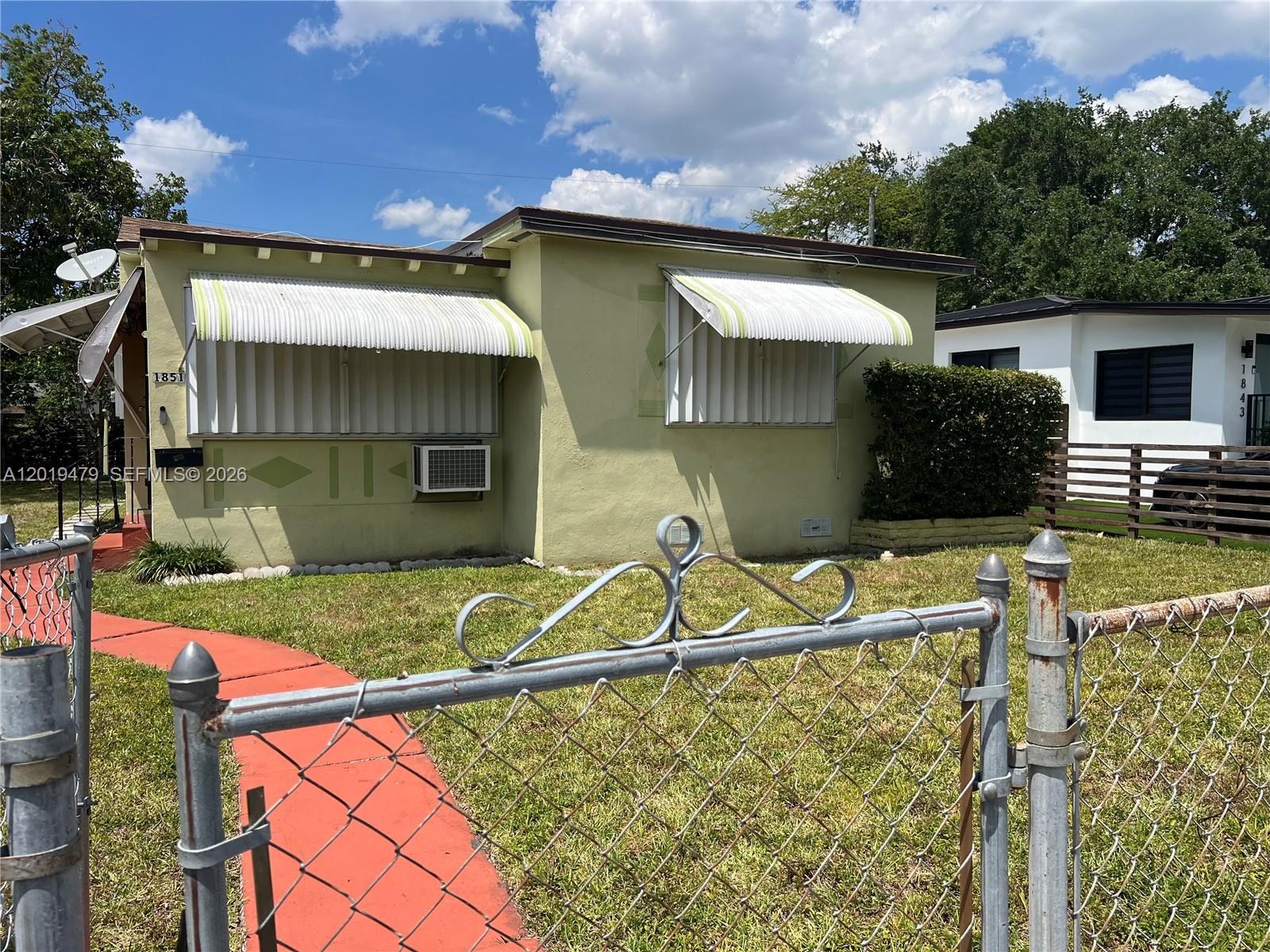 A pale green house with metal awnings and a chain-link fence in the front yard — 1851 NW 51st Ter, Miami FL 33142, MIAMI, FL