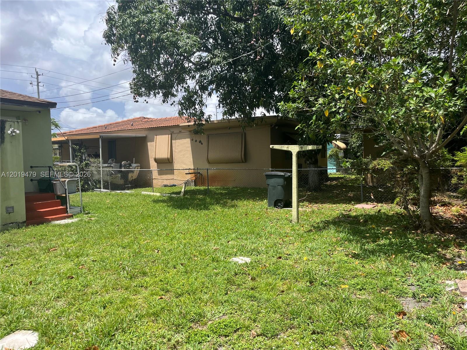 A backyard features a grassy lawn, a chain-link fence, and a single-story house exterior — 1851 NW 51st Ter, Miami FL 33142, MIAMI, FL