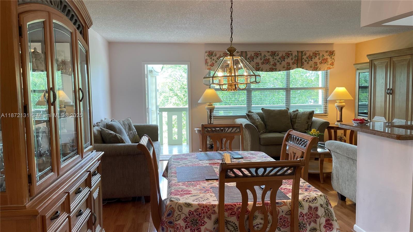 A dining area with a floral tablecloth and hutch opens to a living room with balcony — 3033 Berkshire B # 3033, Deerfield Beach FL 33442, DEERFIELD BEACH, FL