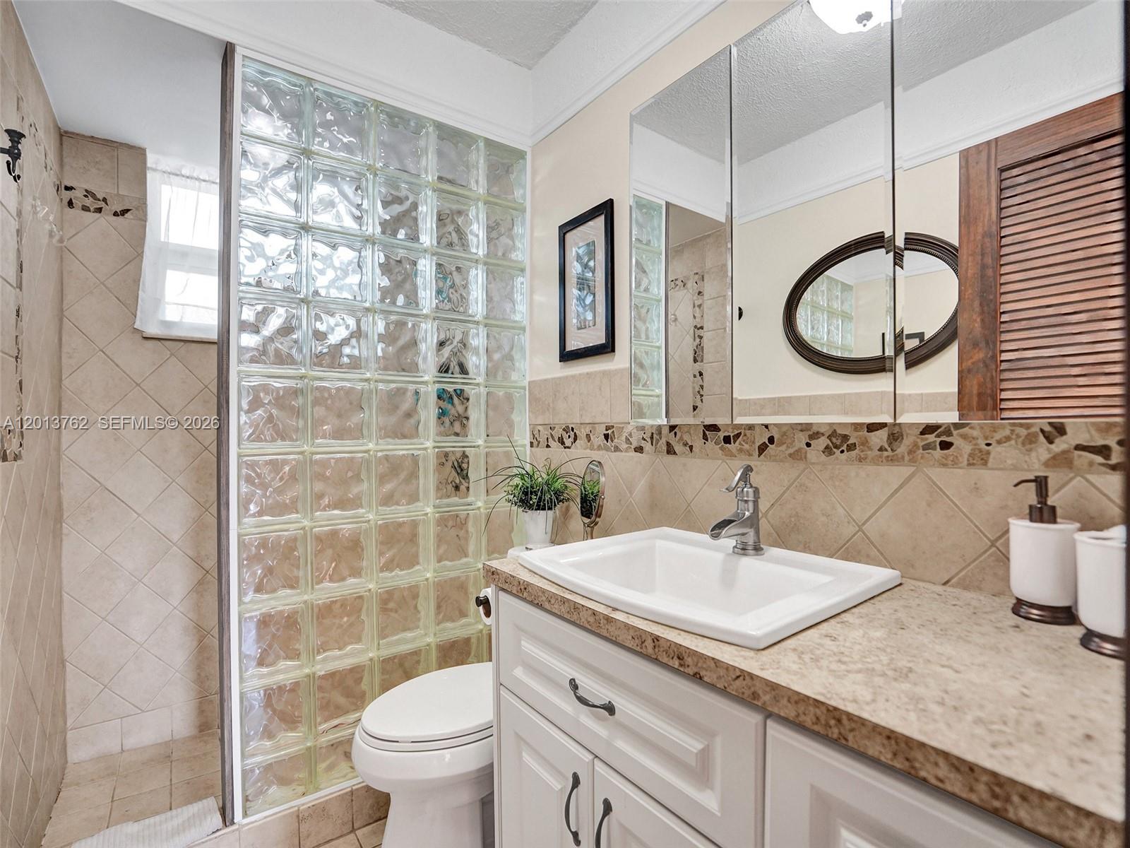 A bathroom features a glass block wall, a white vanity with a sink, and tiled walls — 2600 Diana Dr # 105, Hallandale Beach FL 33009, HALLANDALE BEACH, FL