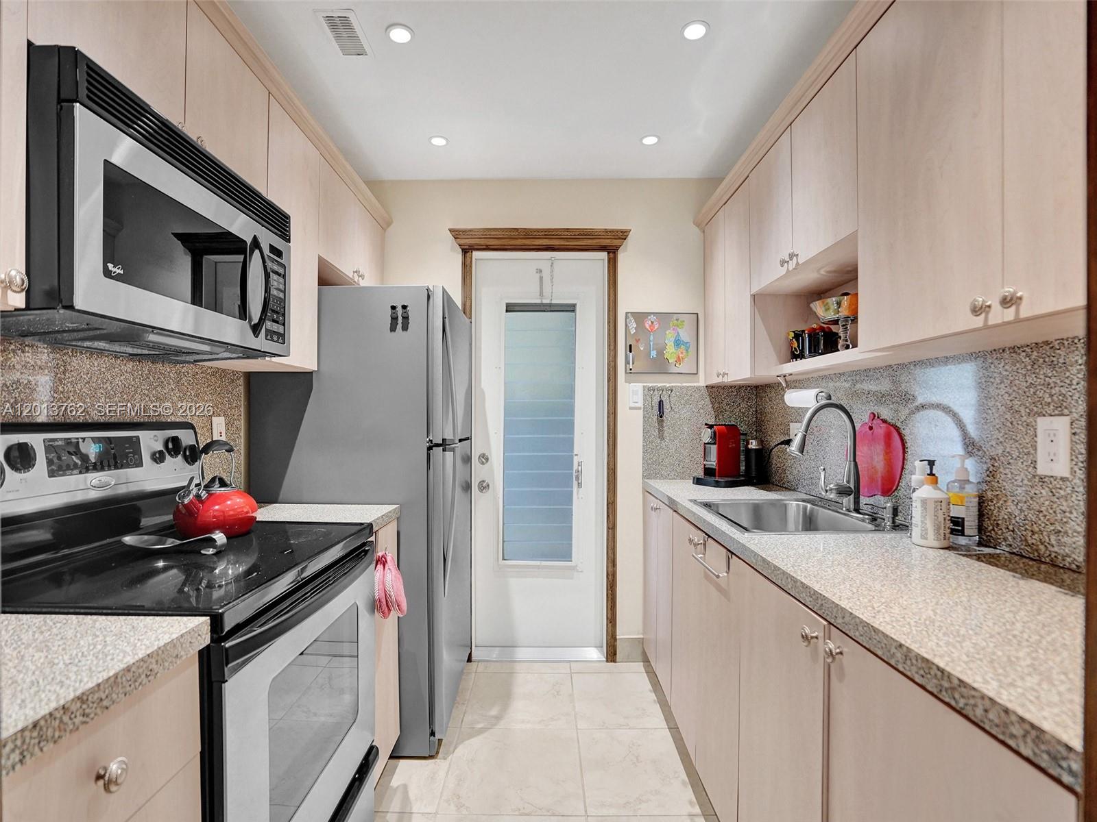 A galley kitchen features light wood cabinets, granite countertops, stainless steel appliances, and a back door — 2600 Diana Dr # 105, Hallandale Beach FL 33009, HALLANDALE BEACH, FL