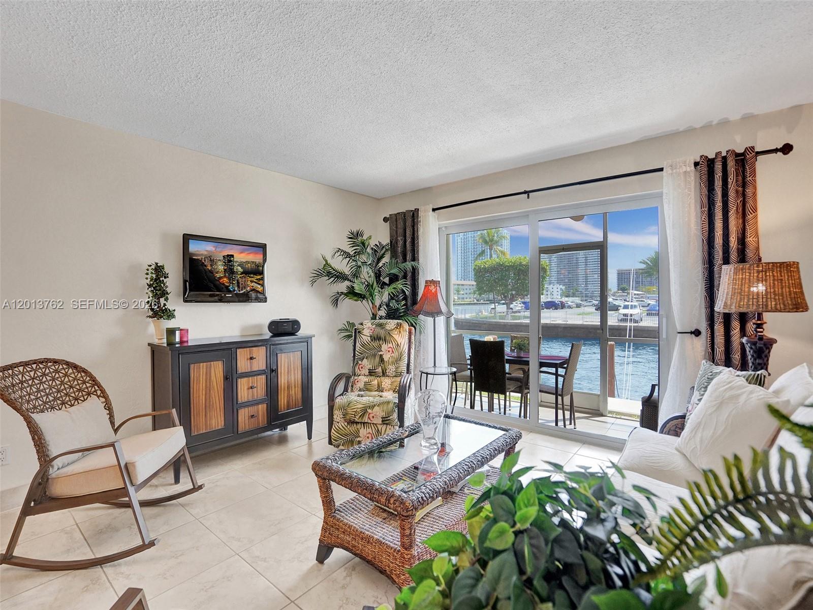 A living room features tile floors, wicker furniture, and a sliding door overlooking a marina — 2600 Diana Dr # 105, Hallandale Beach FL 33009, HALLANDALE BEACH, FL
