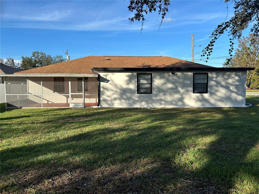 The exterior rear view of a single-story house features a screened-in porch and two windows — 602 MESILLA DRIVE, KISSIMMEE, FL