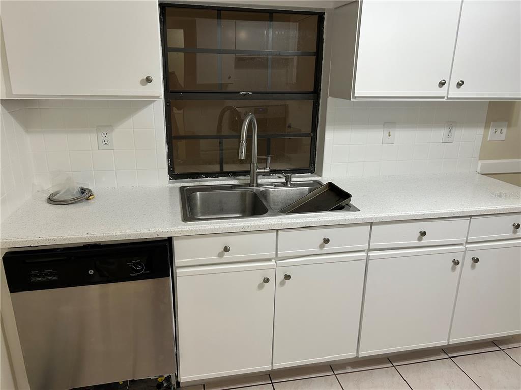 A kitchen features white cabinets, a stainless steel dishwasher, a double sink, and tiled walls — 602 MESILLA DRIVE, KISSIMMEE, FL