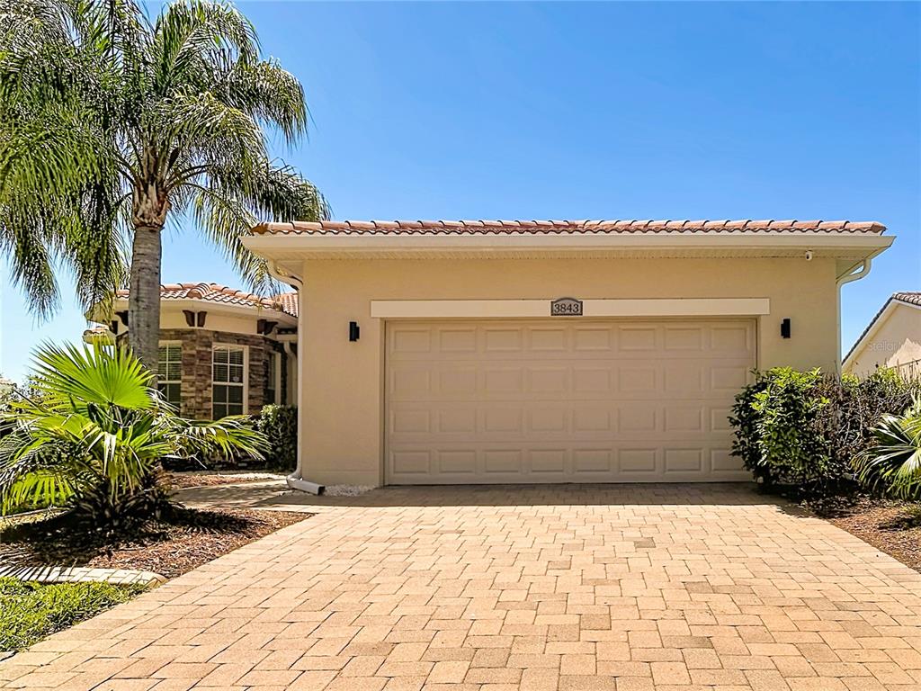 A beige house exterior features a two-car garage, a paver driveway, and a palm tree — 3843 GOLDEN KNOT DRIVE, KISSIMMEE, FL