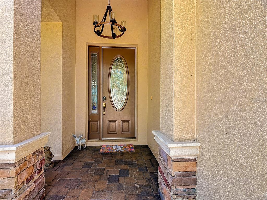 A covered entryway features a brown front door with an oval glass insert and stone-accented pillars — 3843 GOLDEN KNOT DRIVE, KISSIMMEE, FL