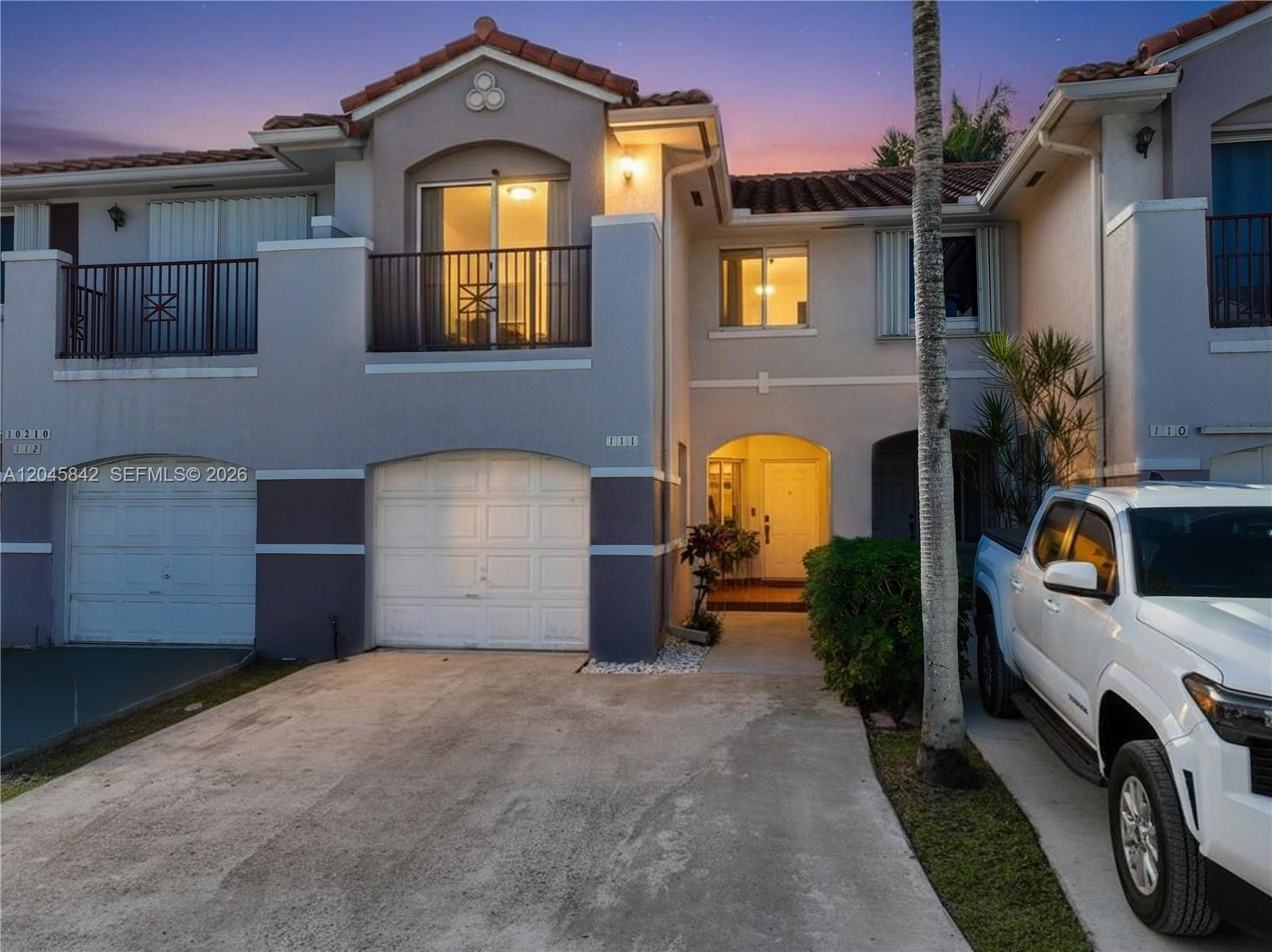 A two-story townhouse exterior features a garage, a balcony, and a white pickup truck parked outside — 10210 SW 154th Pl # 111, Miami FL 33196, MIAMI, FL