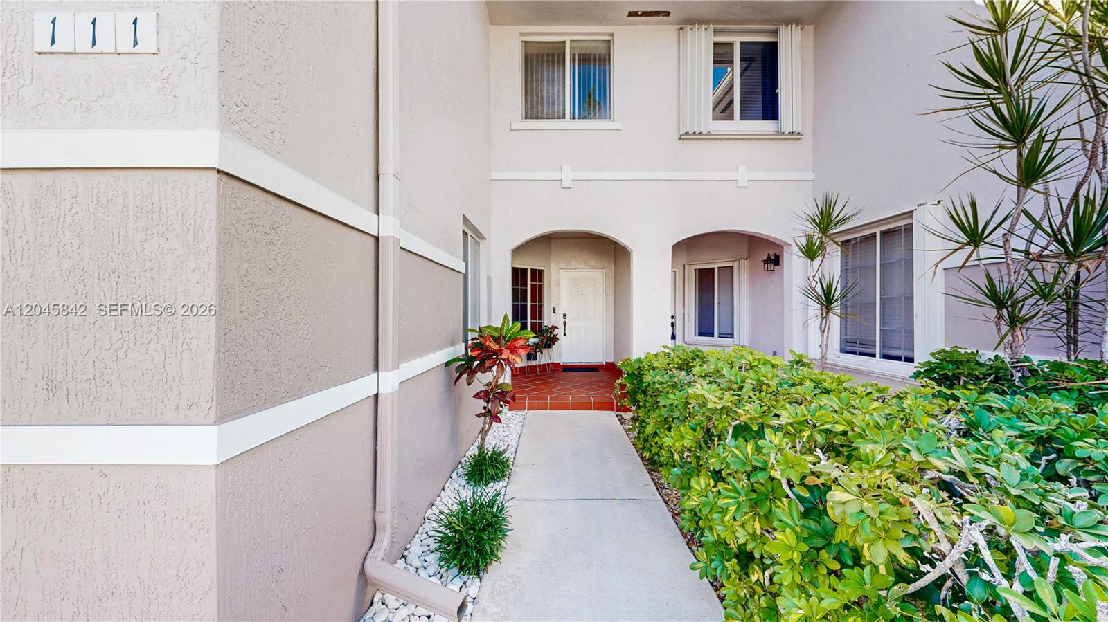A concrete walkway leads to the white front door of a two-story stucco building — 10210 SW 154th Pl # 111, Miami FL 33196, MIAMI, FL