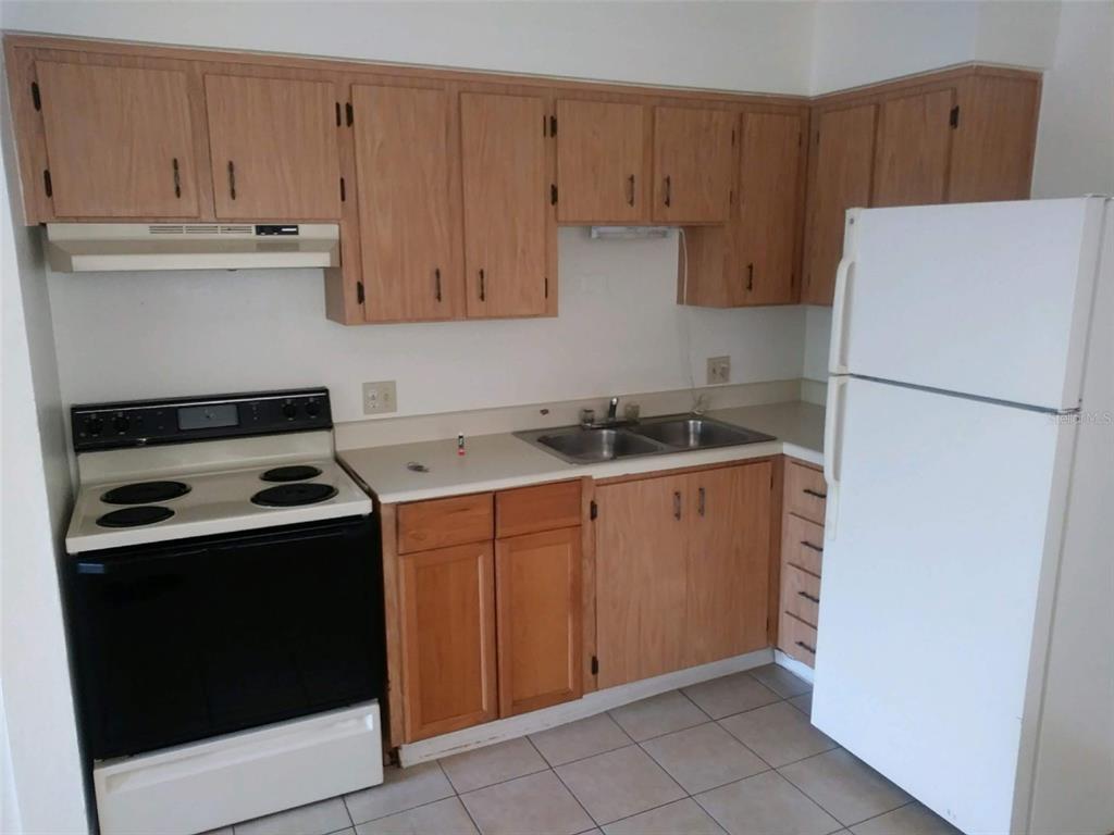 A kitchen features wood cabinets, a white stove, a double sink, and a white refrigerator — 736 MICHIGAN COURT UNIT 4, ST CLOUD, FL