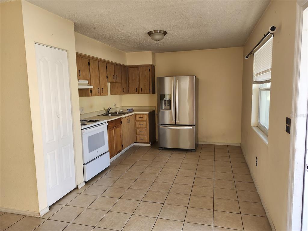 A kitchen with wood cabinets, stainless steel refrigerator, white stove, and beige tile flooring — 736 MICHIGAN COURT UNIT 4, ST CLOUD, FL