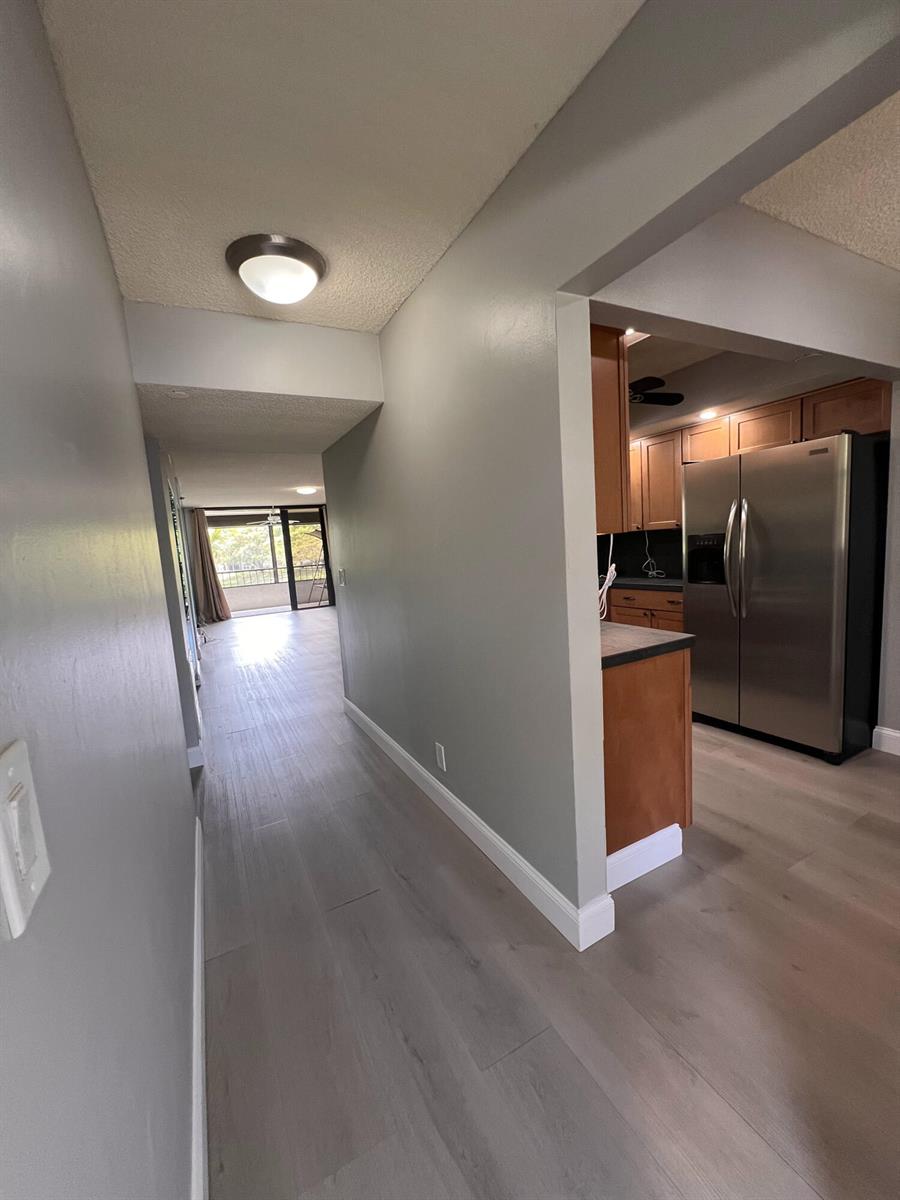 A hallway with light wood flooring leads toward a living area and a kitchen — 1850 Homewood Boulevard, Delray Beach FL 33445, DELRAY BEACH, FL