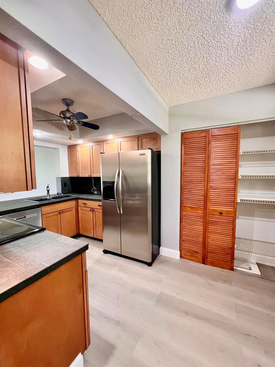 A kitchen features wood cabinets, stainless steel appliances, dark countertops, and a louvered pantry door — 1850 Homewood Boulevard, Delray Beach FL 33445, DELRAY BEACH, FL