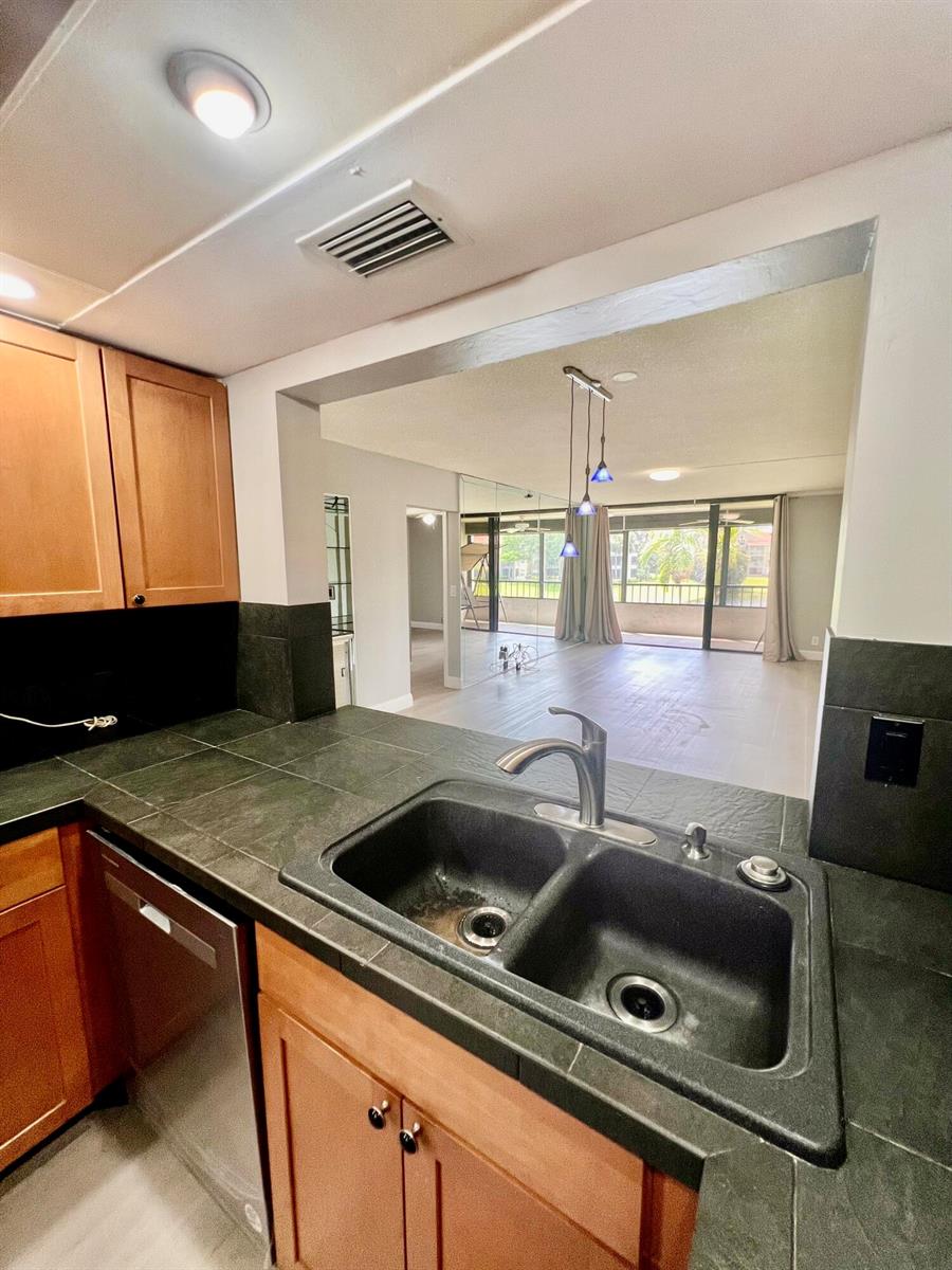 A kitchen with dark tile countertops and a double sink overlooks an open living area — 1850 Homewood Boulevard, Delray Beach FL 33445, DELRAY BEACH, FL