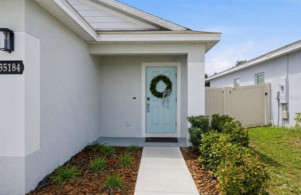 A light blue front door with a wreath is centered under a covered entryway — 35184 ARYA WAY, ZEPHYRHILLS, FL