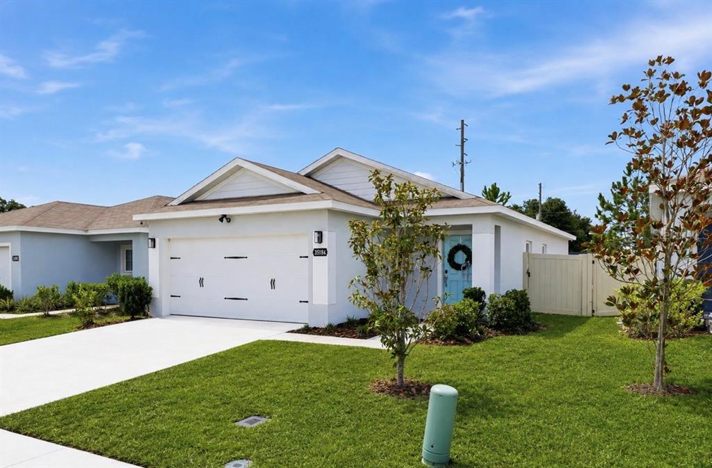 A single-story white house with a two-car garage, light blue front door, and green lawn — 35184 ARYA WAY, ZEPHYRHILLS, FL