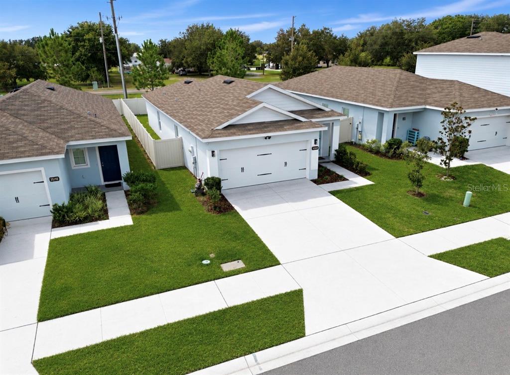 An aerial view shows three adjacent single-story houses with driveways and green lawns — 35184 ARYA WAY, ZEPHYRHILLS, FL