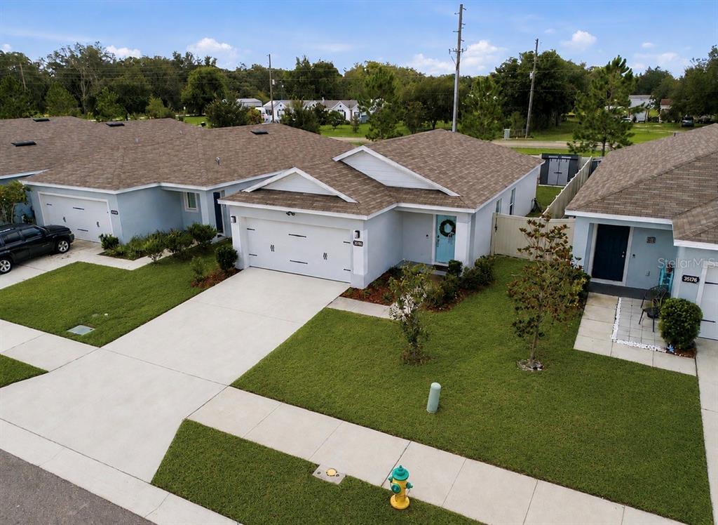 An aerial view shows the exterior of a light blue duplex with a concrete driveway — 35184 ARYA WAY, ZEPHYRHILLS, FL