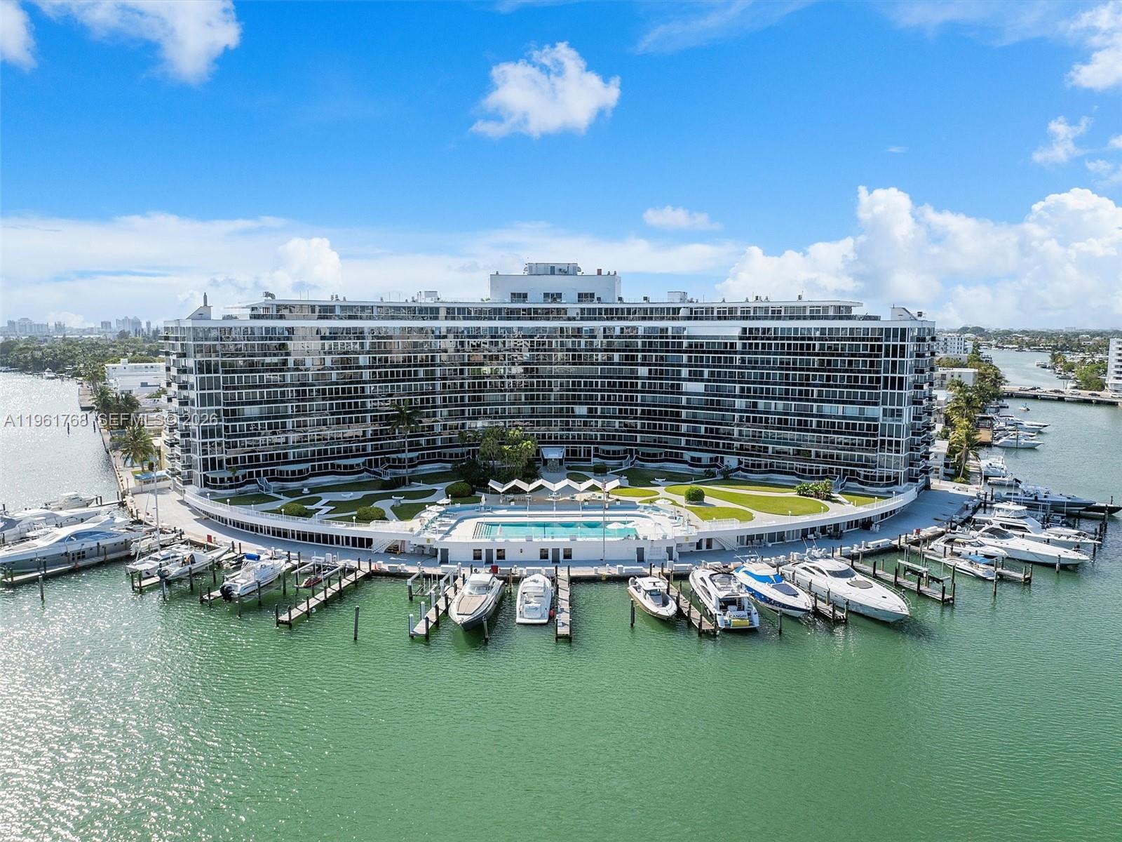 An aerial view shows a large curved residential building with a pool and private marina — 900 Bay Dr # 1012, Miami Beach FL 33141, MIAMI BEACH, FL