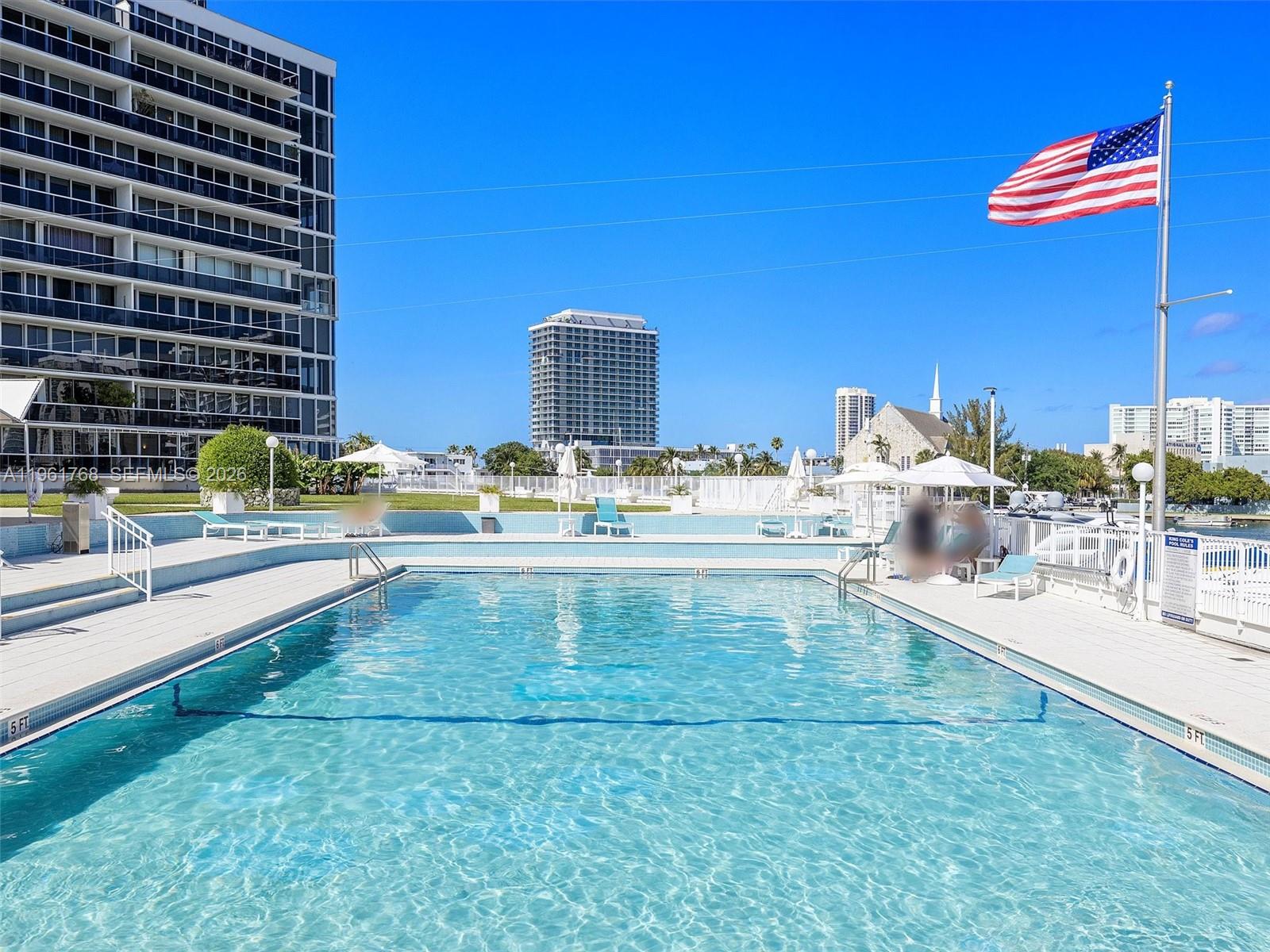 An outdoor swimming pool is surrounded by a deck with lounge chairs and umbrellas — 900 Bay Dr # 1012, Miami Beach FL 33141, MIAMI BEACH, FL